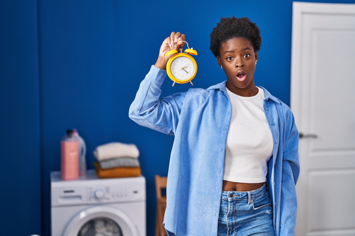 Frau hält einen gelben Wecker in der Hand, im Hintergrund steht eine Waschmaschine