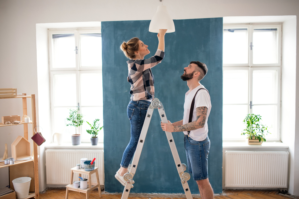 Frau wechselt auf einer Leiter eine LED Birne. Ein Mann hält dabei die Leiter.