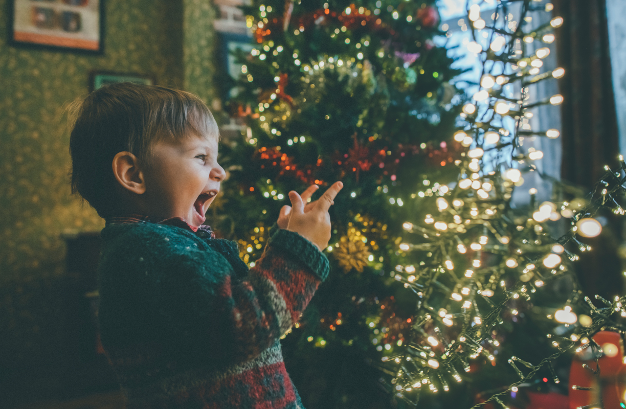 Kind steht vor beleuchteten Weihnachtsbaum und schreit.