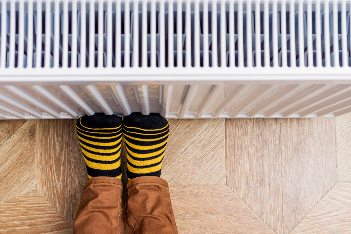 Person, die Füße in hellen gelb-schwarz-Socken gegen einen Heizkörper wärmt