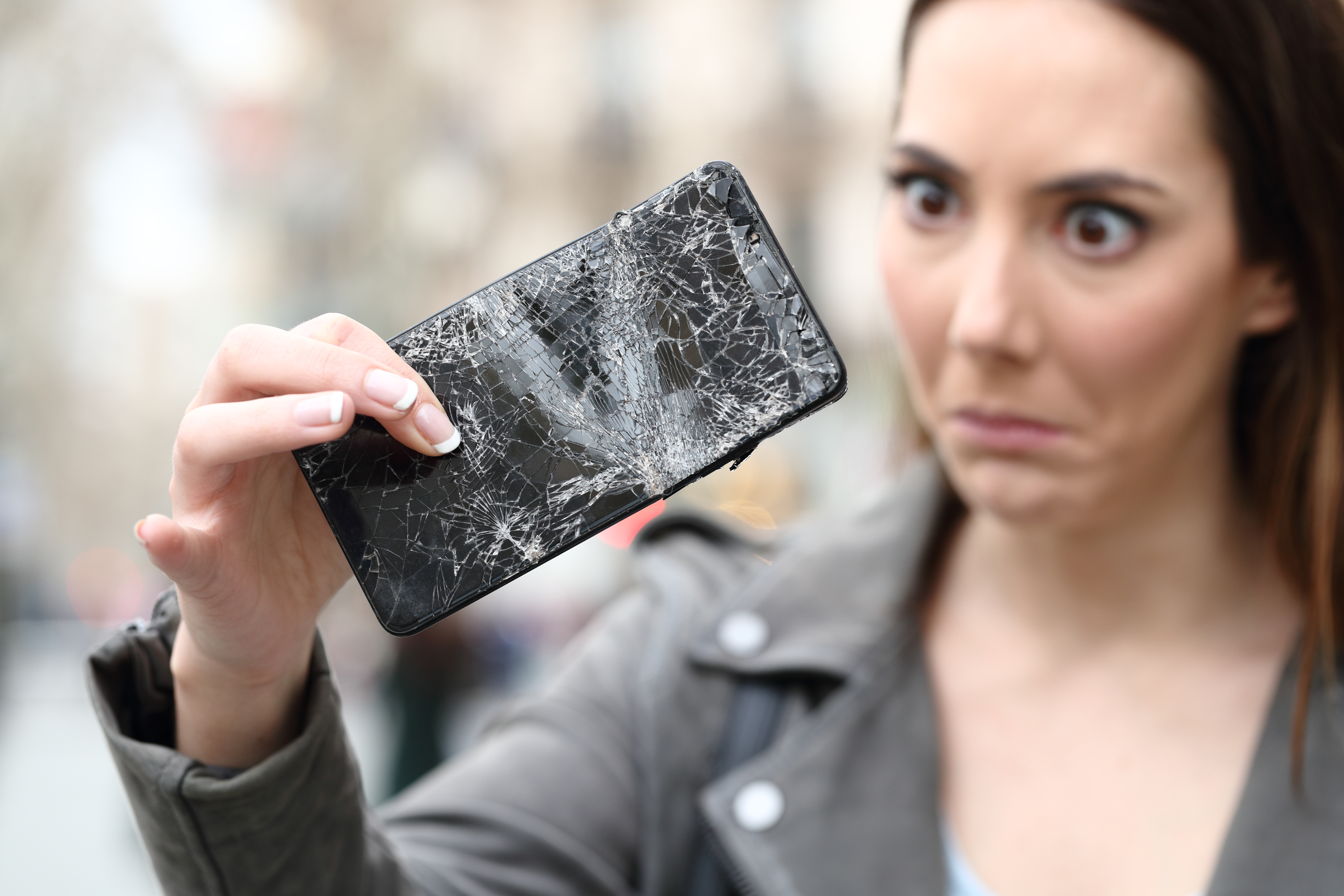 Frau schaut verwundert ihr Smartphone mit gebrochenem Display an